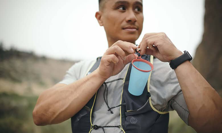An athlete preparing for a run, holding a water bottle with a hydration tube, outdoors in a natural setting.