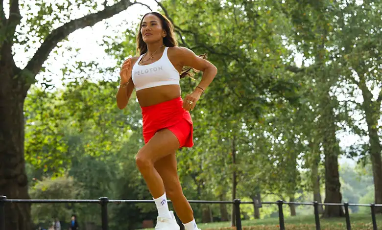An energetic female runner in athletic gear, representing Peloton, running outdoors during the HOKA Hackney Half Marathon, highlighting collaboration between Peloton and the event.
