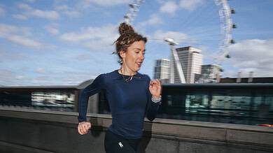 Female runner in athletic gear running along a riverbank with the London Eye in the background on a clear day.