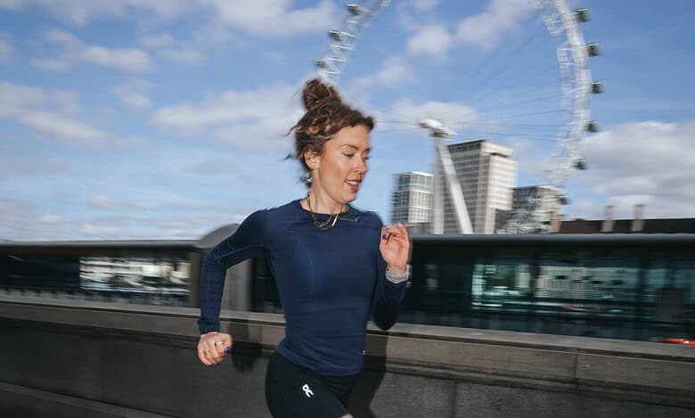Female runner in athletic gear running along a riverbank with the London Eye in the background on a clear day.