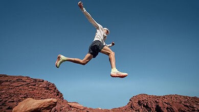 A trail runner in mid-air jump over rocky terrain during outdoor run, showcasing agility and endurance in nature.