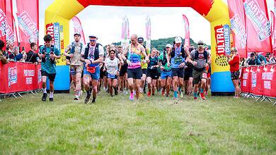 Runners start the Peak District Ultra Challenge at the starting line under a red and yellow inflatable arch.