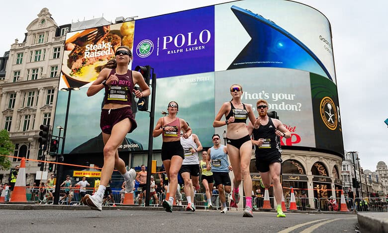 Group of runners participating in the London 10K race, with iconic Trafalgar Square buildings and digital advertising billboards in the background.