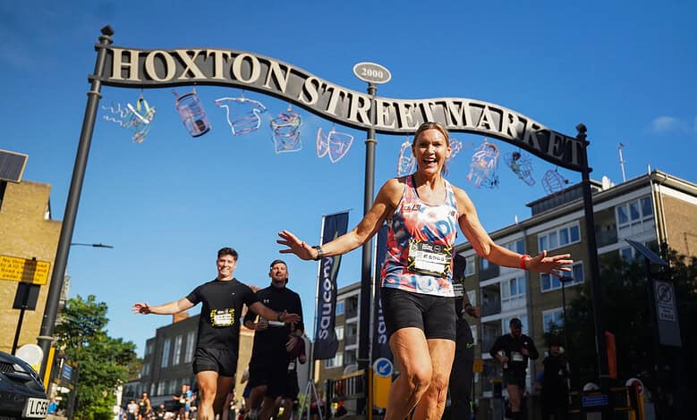Female runner celebrating crossing the finish line at Hoxton Street Market during Saucony Run Shoreditch Half 2026 event.