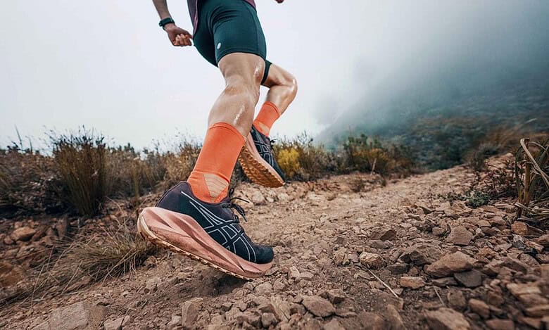 Runner in trail shoes and orange socks running on a rugged mountain trail with misty background.