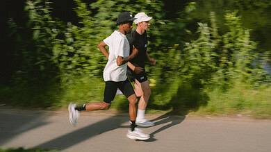 Two runners, a man and a woman, jogging along a scenic riverside path surrounded by lush greenery.