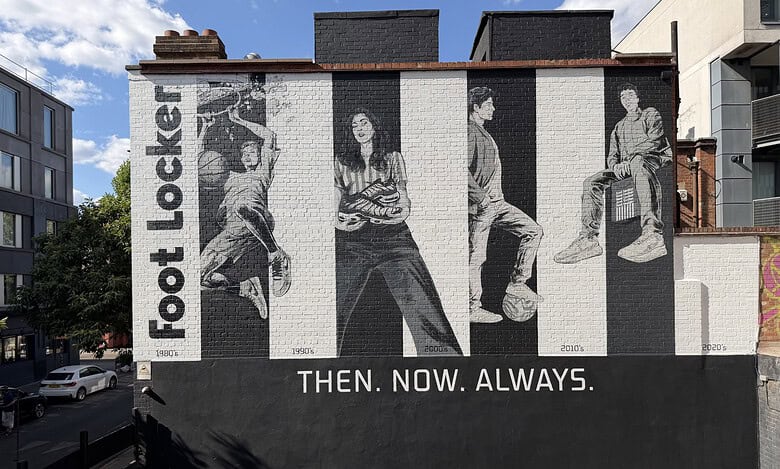 Black and white mural of four people sitting and standing, with 'Foot Locker' text and 'Then. Now. Always.' slogan on a city wall.