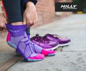 Close-up of a person putting on purple and pink running socks with purple running shoes in the background, on a city sidewalk.