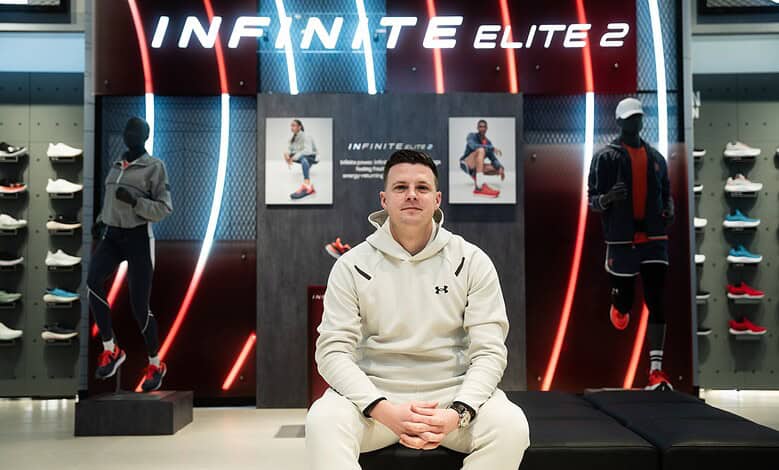 Jonathan Hutnyan sitting in front of Under Armour Infinite Elite 2 running shoes display at a store.
