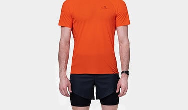 Male runner in orange t-shirt, black shorts, white socks, and running shoes, standing against a plain white background.