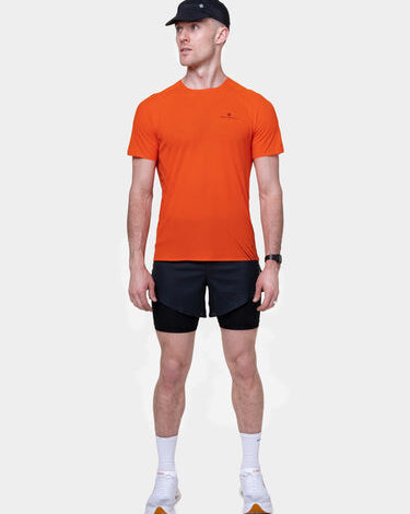 Male runner in orange t-shirt, black shorts, white socks, and running shoes, standing against a plain white background.