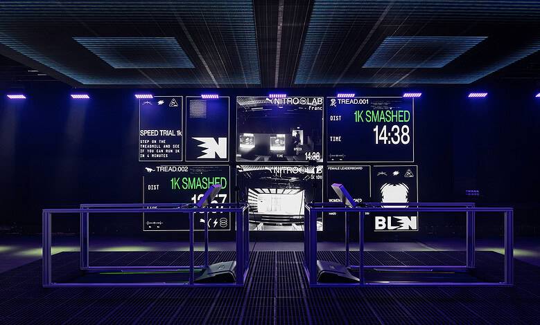 Futuristic indoor running track with digital screens displaying race times and stats, illuminated by blue and purple LED lights.