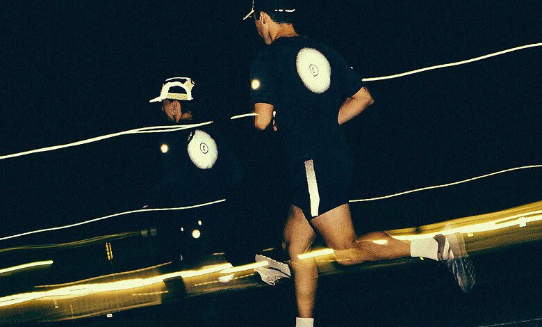 Two runners running at night on a track, illuminated by headlamps and reflective gear, with a dark background and motion blur.