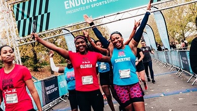 Happy female runners crossing the finish line at the Endure Relays event, celebrating their achievement with arms raised, in a vibrant outdoor setting.