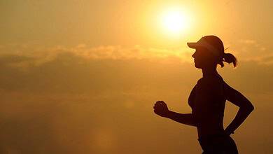 Silhouette of a runner wearing a cap during a sunrise run against a warm, golden sky.