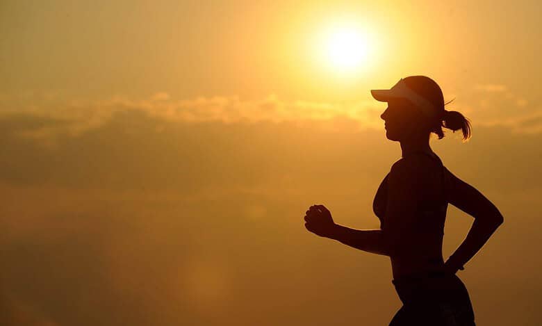 Silhouette of a runner wearing a cap during a sunrise run against a warm, golden sky.