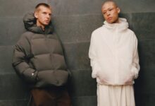 Two models wearing winter outerwear from adidas and Arte Antwerp's FW26 collection, standing against a dark wall.