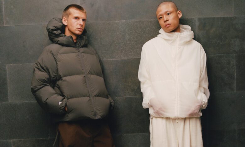 Two models wearing winter outerwear from adidas and Arte Antwerp's FW26 collection, standing against a dark wall.