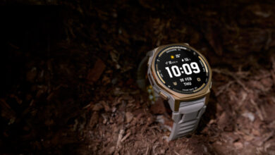 Rugged smartwatch with a round display resting on rocky trail terrain, illuminated by a beam of light.