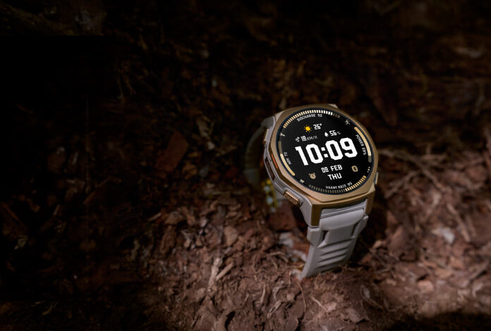 Rugged smartwatch with a round display resting on rocky trail terrain, illuminated by a beam of light.