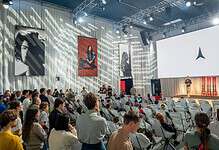 Audience attending a Running Insights conference with a speaker on stage and large screens displaying the Running Insights logo.