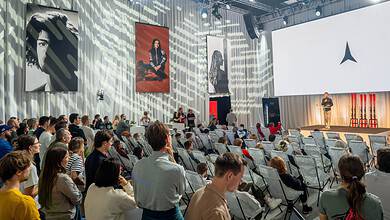 Audience attending a Running Insights conference with a speaker on stage and large screens displaying the Running Insights logo.