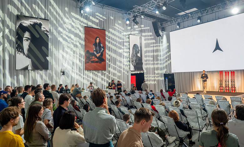Audience attending a Running Insights conference with a speaker on stage and large screens displaying the Running Insights logo.