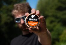 Man holding Bearhug Anti Chafe Rub container towards camera with blurred background.