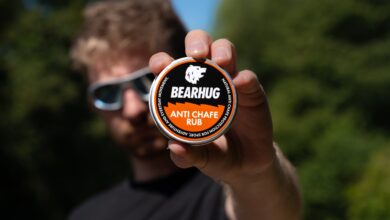 Man holding Bearhug Anti Chafe Rub container towards camera with blurred background.