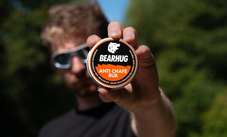 Man holding Bearhug Anti Chafe Rub container towards camera with blurred background.