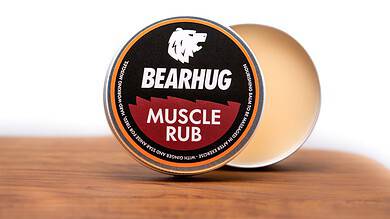 Bearhug Muscle Rub tin on a wooden surface with a blurred background, product label clearly visible.