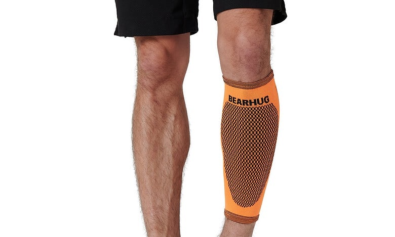 Orange Bearhug compression sleeve on a man's lower leg, knee to ankle, showing a dotted pattern and branding.