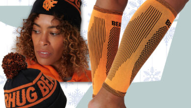 Person wearing orange knee-high socks and two knit beanies with pom-poms, set against a pale blue background with snowflake patterns.