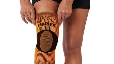 Athlete wearing an orange knee sleeve labeled Bearhug on a kneeling leg with black compression socks.