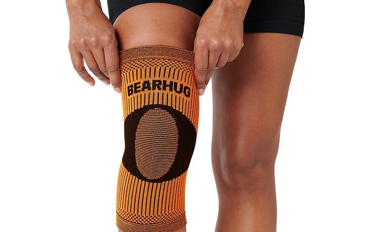 Athlete wearing an orange knee sleeve labeled Bearhug on a kneeling leg with black compression socks.