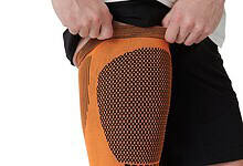 Athletic knee sleeve in orange with a dotted pattern, worn by a runner to support the knee during training.