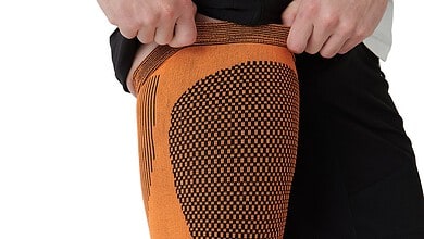 Athletic knee sleeve in orange with a dotted pattern, worn by a runner to support the knee during training.