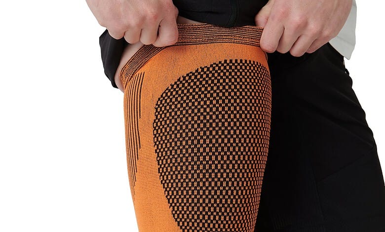 Athletic knee sleeve in orange with a dotted pattern, worn by a runner to support the knee during training.