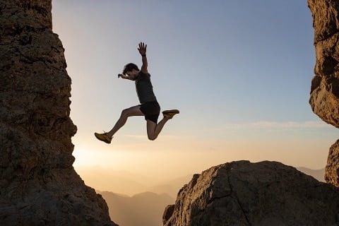 Runner leaping between rocky cliffs at sunset, showcasing athletic movement and endurance.