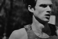 Black and white image of a male runner with a focused expression, wearing a Nike sports top, captured during a race or training session.