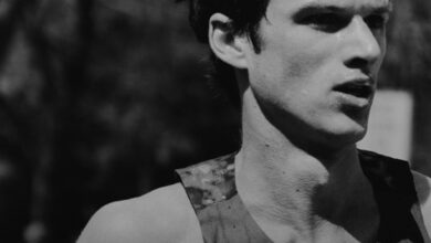Black and white image of a male runner with a focused expression, wearing a Nike sports top, captured during a race or training session.