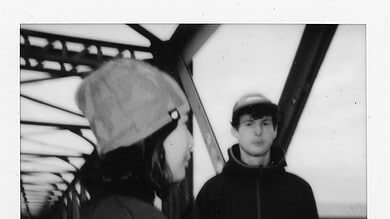 Two young runners, a girl and a boy, standing on a bridge during a running event, with the girl wearing a cap and the boy in a hoodie, in black and white.