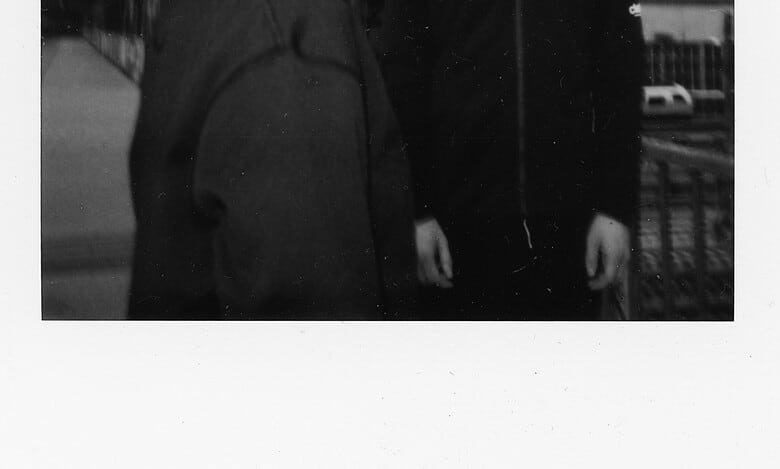 Two young runners, a girl and a boy, standing on a bridge during a running event, with the girl wearing a cap and the boy in a hoodie, in black and white.