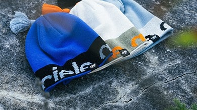 Blue, white, and grey beanie with orange accents on a rocky surface, featuring the Running Insights branding along the cuff.