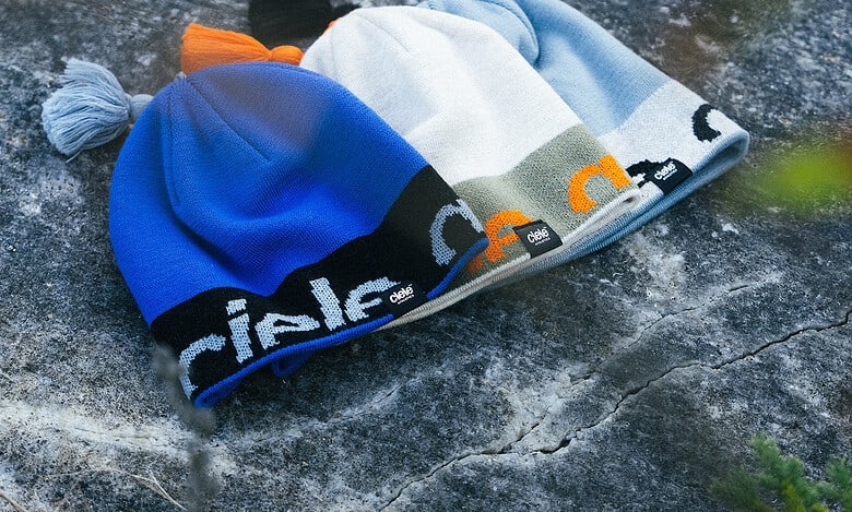 Blue, white, and grey beanie with orange accents on a rocky surface, featuring the Running Insights branding along the cuff.