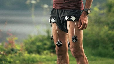 Male runner in outdoor landscape checking his smartphone, with running devices attached to his shorts, mountains in the background.