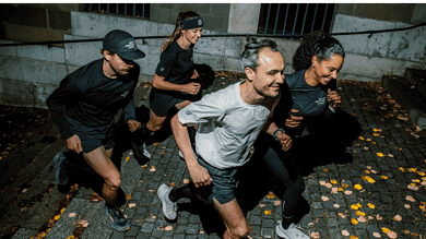 Group of four runners training together at night on a cobblestone street, wearing athletic gear, with fallen leaves around, promoting night running fitness.