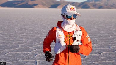 Runner in Red Bull gear exploring salt flats with mountains in the background, wearing sunglasses and a hat, capturing the adventurous spirit of outdoor running.