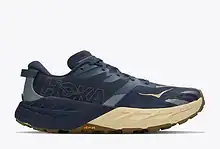 HOKA trail running shoe in navy and beige with Vibram sole, designed for comfort and durability during outdoor runs.