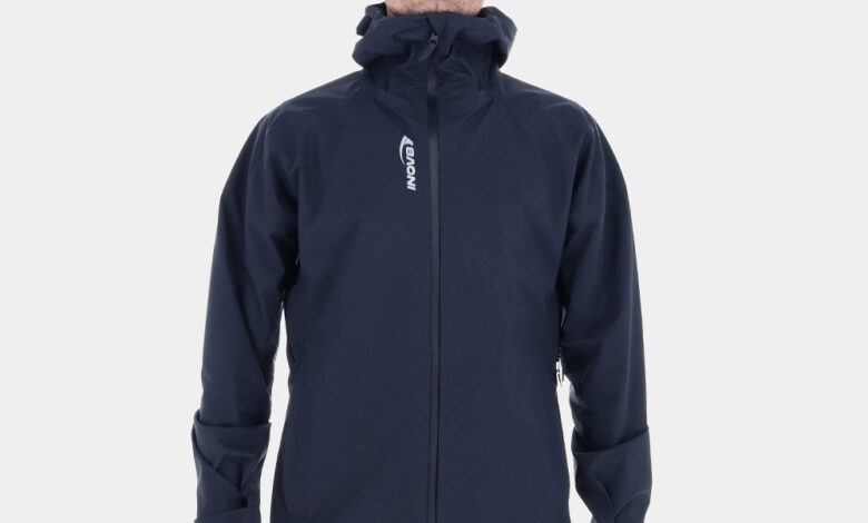 Man wearing INOV8 VentureShell waterproof jacket with hood, designed for wet-weather outdoor activities.
